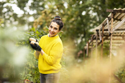 Lächelnde Frau mit Gemüse in der Hand in einem städtischen Garten - SGF02686