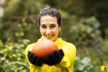 Smiling woman holding pumpkin in hand while standing at urban garden - SGF02690