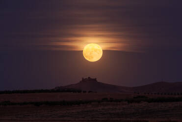 Hellgelber Mond leuchtet am Nachthimmel über einem entfernten Schloss und Feldern auf dem Lande - ADSF15960