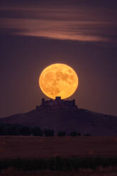 Hellgelber Mond leuchtet am Nachthimmel über einem entfernten Schloss und Feldern auf dem Lande - ADSF15961