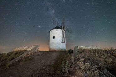 Low angle of old white windmill tower located on hill against starry night sky with Milky Way - ADSF15962