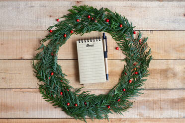 Draufsicht auf Stift zu schreiben festliche Menü in Notebook platziert innerhalb Weihnachtskranz auf Holztisch - ADSF15968