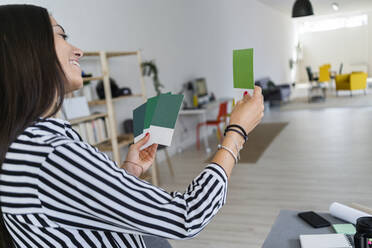 Lächelnde Designerin, die in einem Architekturbüro eine Farbpalette auswählt - GIOF08970