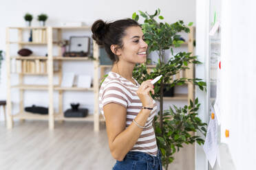 Smiling young businesswoman looking at whiteboard while working at office - GIOF08997