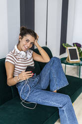 Lächelnde Architektin sitzt mit Smartphone auf dem Sofa im Kreativbüro in der Pause - GIOF09009