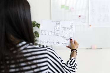 Female architect analyzing floor plan on paper at creative workplace - GIOF09025