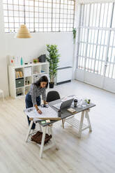 Selbstbewusste Geschäftsfrau arbeitet an einem Entwurf am Schreibtisch in einem kreativen Büro - GIOF09033