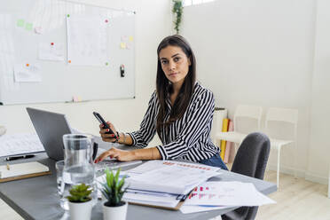 Selbstbewusste Designerin sitzt mit drahtlosen Technologien am Schreibtisch im Büro - GIOF09038