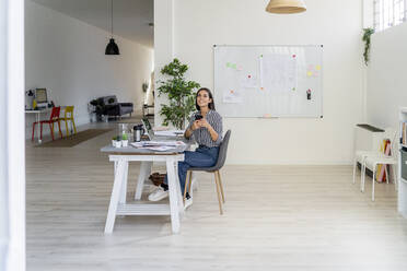 Junge Designerin, die ihr Smartphone in der Hand hält und zu einem kreativen Büro aufschaut - GIOF09041