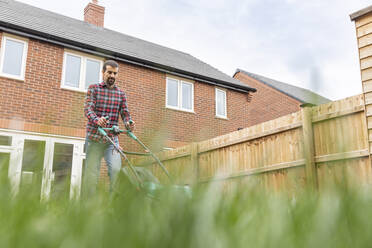 Man mowing lawn with lawn mower at backyard - WPEF03418