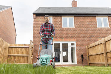 Mid adult man using lawn mower for mowing at backyard - WPEF03419