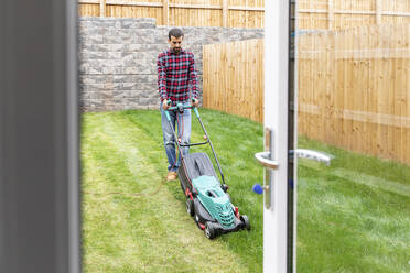 Mann beim Rasenmähen mit Rasenmäher im Hinterhof - WPEF03421