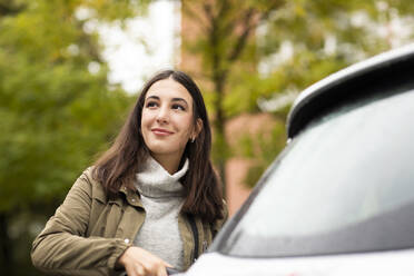 Beautiful woman charging rented electric car while smiling and looking away - SGF02693