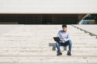 Confident young man using laptop while sitting on steps during sunny day - ABZF03341