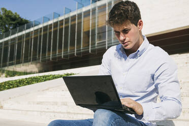 Handsome young man using laptop on sunny day - ABZF03342