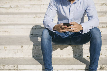 Man surfing internet through smart phone while sitting on steps during sunny day - ABZF03348