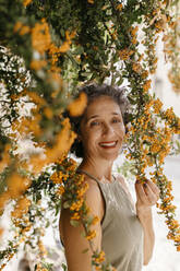 Reife Frau berührt Orangenbaum an einem sonnigen Tag - TCEF01174
