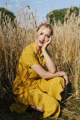 Schöne blonde Frau hockt gegen Pflanzen auf einem Feld an einem sonnigen Tag - RDGF00209