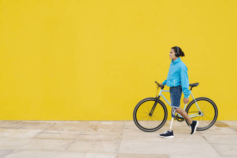 Man with artificial limb and foot walking with bicycle against yellow wall stock photo