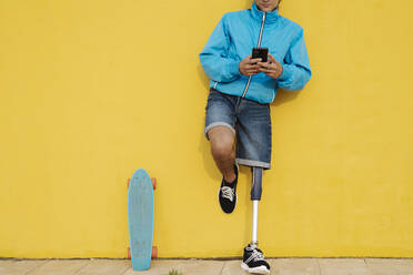 Behinderter Mann, der telefoniert, während er mit dem Skateboard gegen eine gelbe Wand fährt - JCZF00265