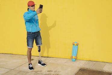 Mann mit Mütze, der ein Selfie macht, während er an einer gelben Wand steht - JCZF00266