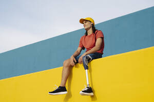 Young man smiling while sitting on wall against clear sky - JCZF00279