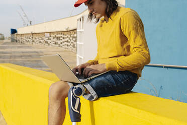 Young man working on laptop while sitting on wall - JCZF00291