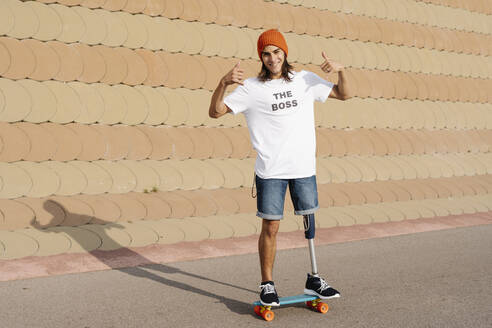 Junger behinderter Mann steht auf einem Skateboard auf dem Sportplatz - JCZF00299
