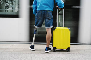 Young man with artificial limb and foot standing by luggage at railroad station - JCZF00323