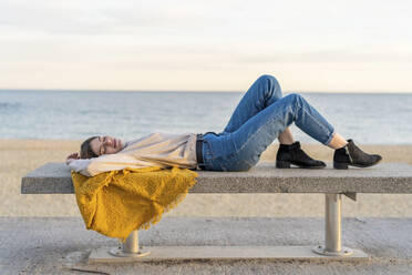 Junge Frau liegt auf einer Bank an der Strandpromenade bei Sonnenuntergang - AFVF07290