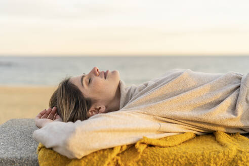 Junge Frau entspannt sich auf einer Bank an der Strandpromenade bei Sonnenuntergang - AFVF07291