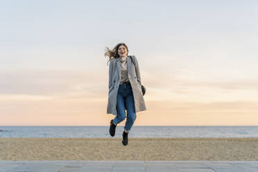 Verspielte junge Frau springt auf der Promenade am Strand gegen den Himmel bei Sonnenuntergang - AFVF07296