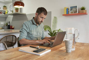 Handsome male freelancer using laptop at dining table while working from home - VEGF02976