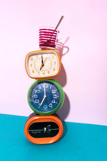 Coffee cup kept over clock stack against blue and pink background - GEMF04190