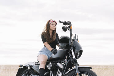 Junge Frau auf Motorrad sitzend gegen den Himmel - DAMF00509
