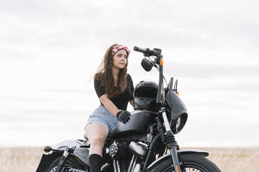 Young woman sitting on motorbike against sky - DAMF00509