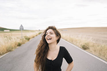 Smiling young woman standing on road against sky - DAMF00510