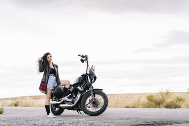 Young female biker standing on road with motorbike - DAMF00512