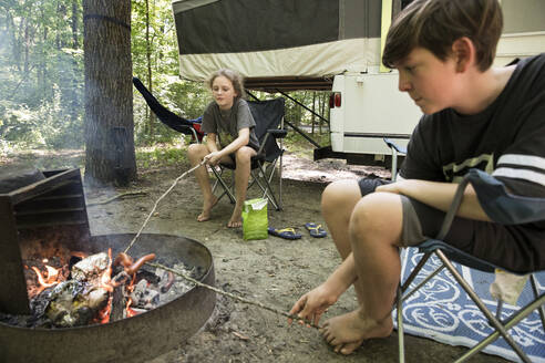 Zwillingsgeschwister auf Familien-Campingausflug braten Hot Dogs über dem Lagerfeuer - CAVF89744