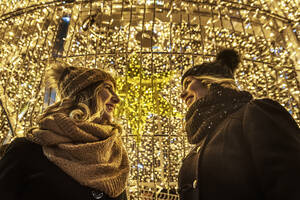 Zwei junge Mädchen lachen im Hintergrund der Weihnachtsbeleuchtung - CAVF89761