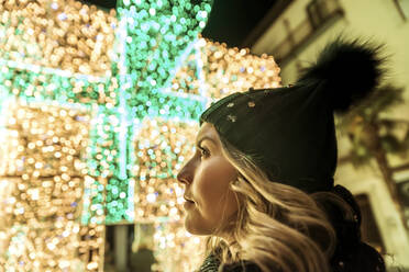 A young girl in a hat looking through Christmas lights - CAVF89762