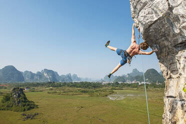 Male climber hanging sideways on overhanging rock in Yangshuo / China - CAVF89769