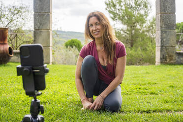 Yogalehrer, der während eines Online-Kurses auf sein Handy schaut, während er im Hinterhof sitzt - DLTSF01295