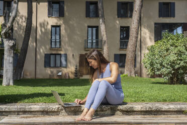 Frau arbeitet am Laptop, während sie im Hinterhof sitzt - DLTSF01300