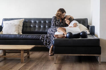 Mother embracing daughter while resting on sofa at home - DLTSF01319