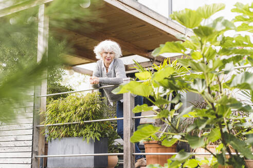 Reife Frau lehnt sich an ein Geländer, während sie zu Hause steht - UUF21596