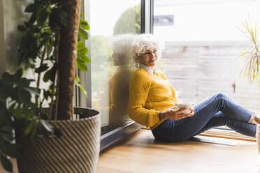 Mature woman sitting with coffee cup at home - UUF21610