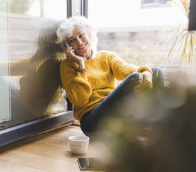 Reife Frau, die zu Hause sitzt und mit ihrem Smartphone spricht - UUF21614