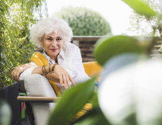 Lächelnde Frau sitzt auf einem Sofa auf dem Balkon - UUF21618