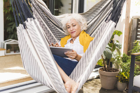 Mature woman using digital tablet while sitting on hammock at home stock photo